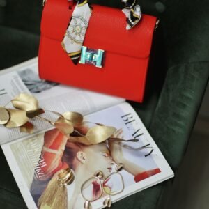 Stylish red handbag with golden accents atop a fashion magazine, ideal for a modern fashion backdrop.
